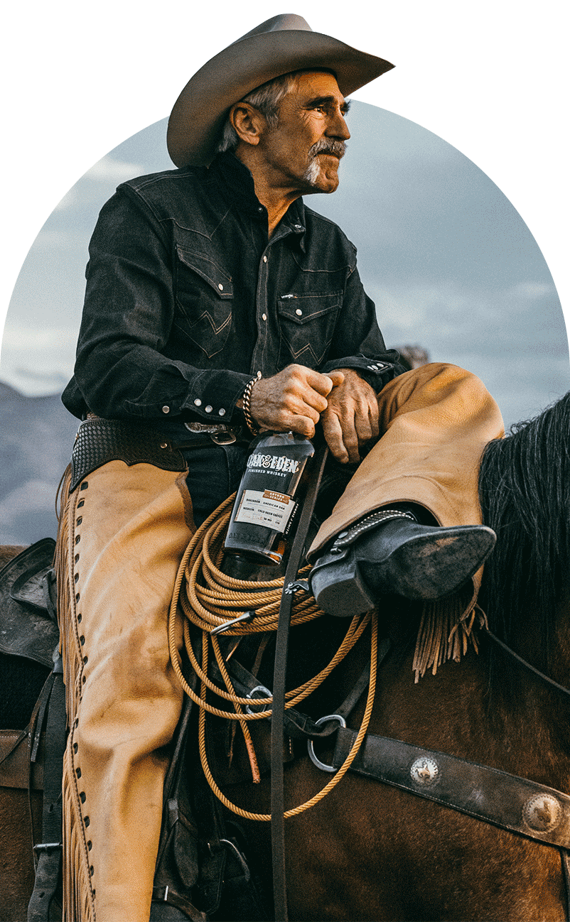 Forrie J Smith wearing a cowboy hat and chaps sitting on a horse looking off into the distance, holding his Oak & Eden Cold Brew Coffee Infused whiskey bottle. 