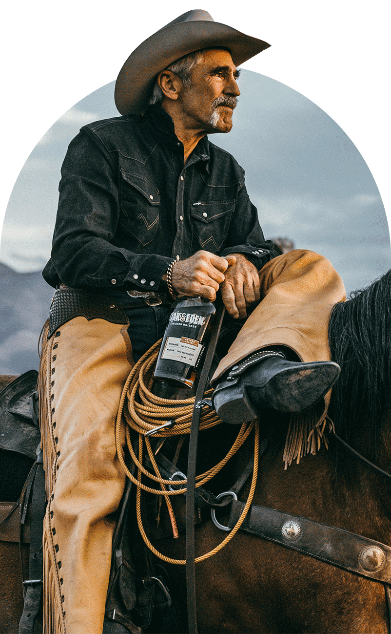 Forrie J Smith wearing a cowboy hat and chaps sitting on a horse looking off into the distance, holding his Oak & Eden Cold Brew Coffee Infused whiskey bottle.